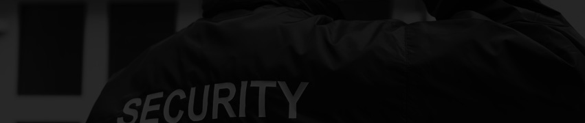 Darkened image of a security guard in a black jacket with “SECURITY” on the back, standing outside a building.